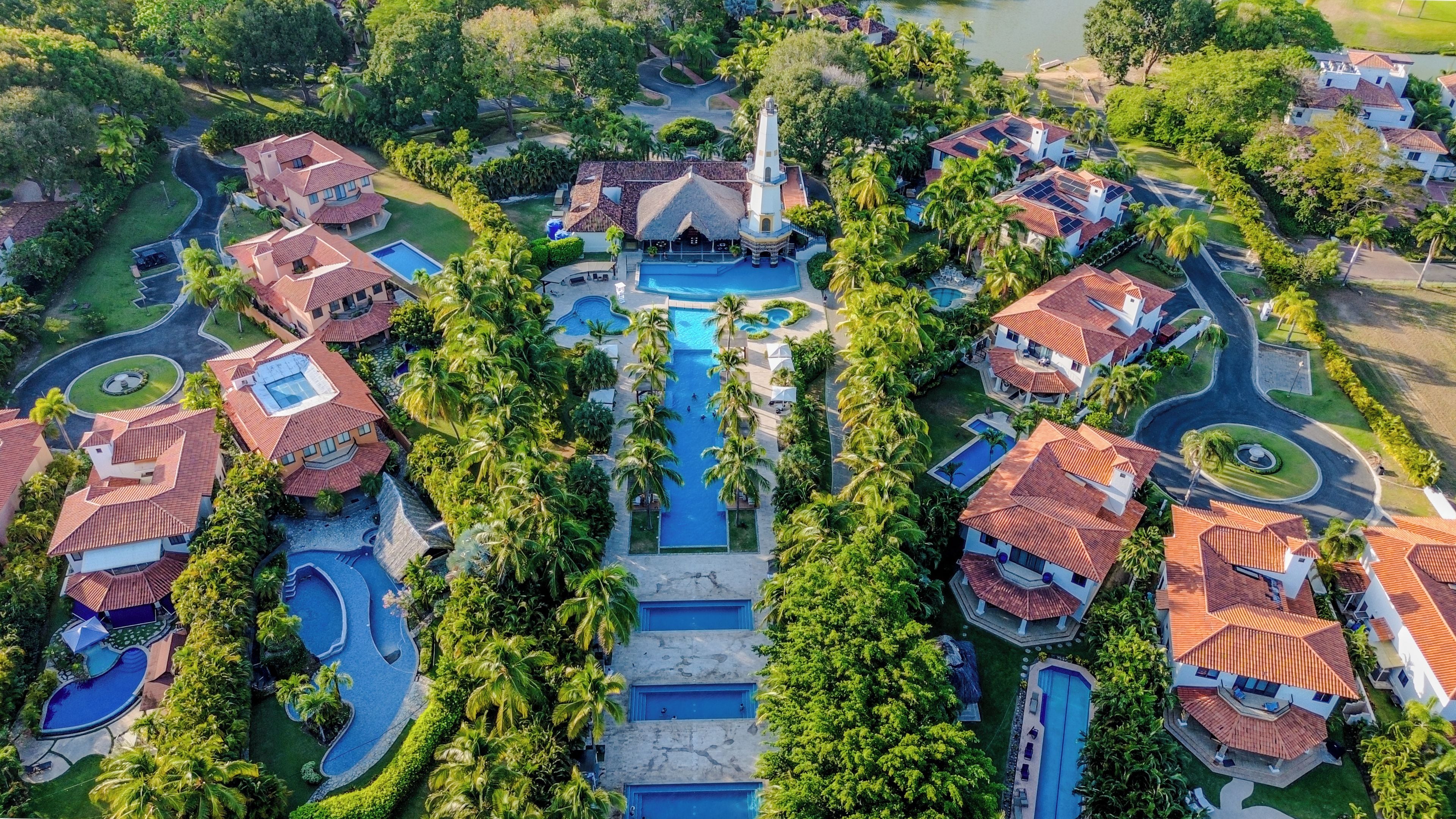 An aerial view of a resort with multiple villas, a central pool, and surrounding greenery.
