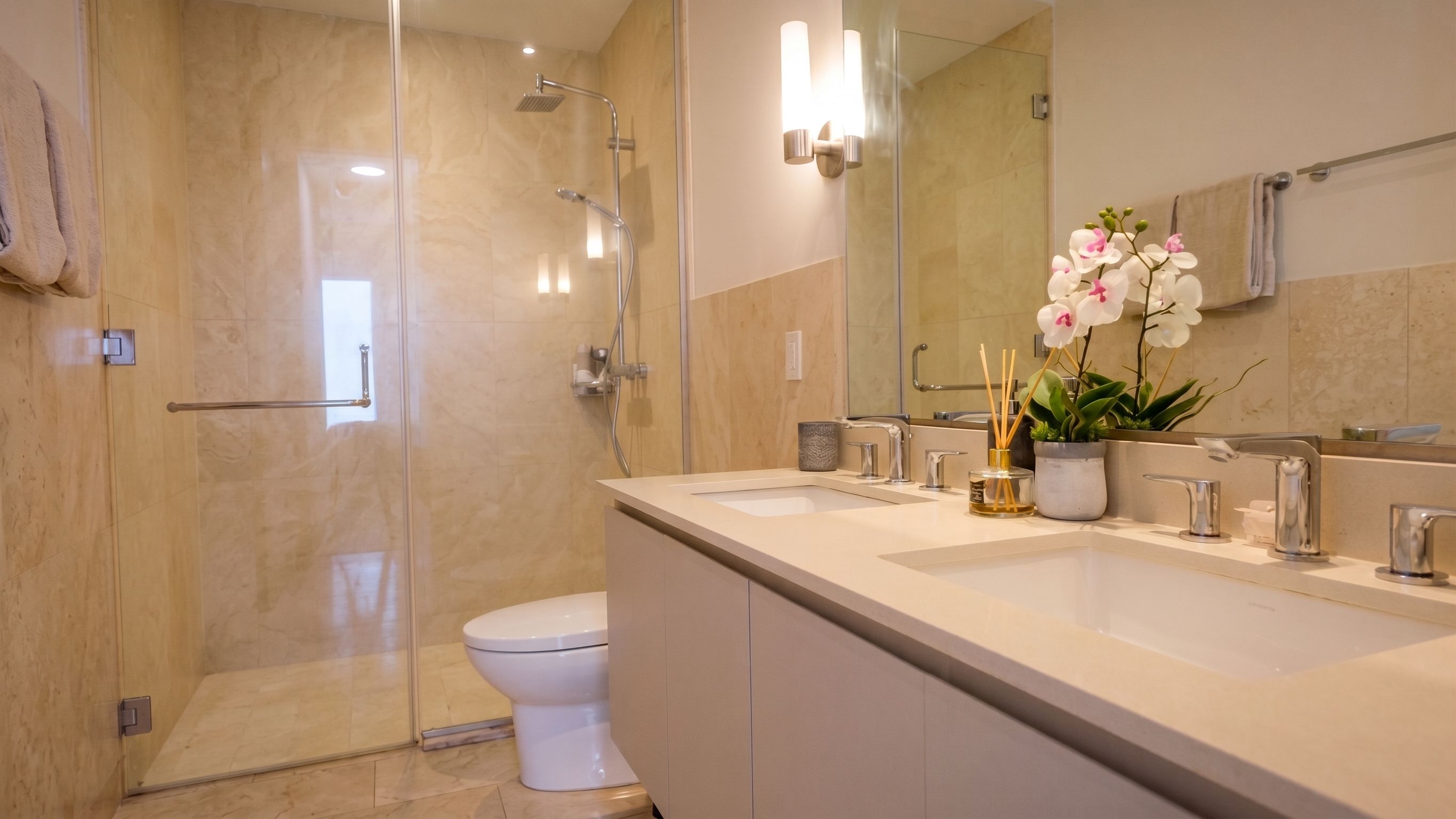 Un bagno moderno con box doccia in vetro, un water, un lavabo con specchio e un'orchidea in vaso.