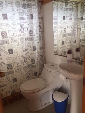 A bathroom with a toilet, sink, and shower curtain featuring vintage stamps. - Cabañas del Faro (Licantén)