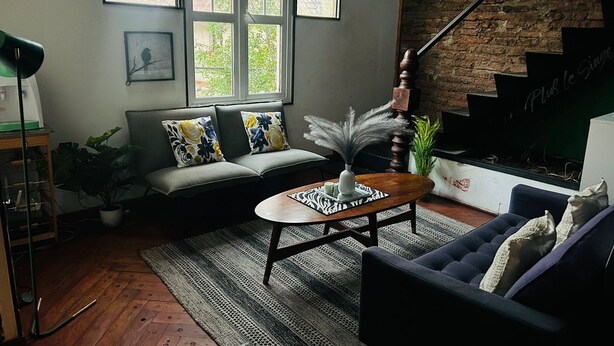 Ein Wohnzimmer mit einer Couch, einem Couchtisch, einer Treppe und einer Ziegelwand.