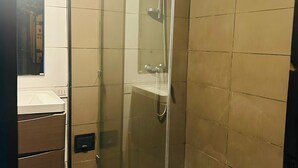 Eine Duschkabine mit Glas, eine Handbrause, ein weißes Waschbecken mit Spiegel darüber und ein Musterboden.