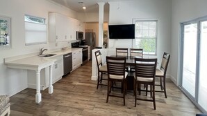Una cocina moderna con armarios blancos, un comedor con sillas de madera y un amplio ventanal que proporciona luz natural.