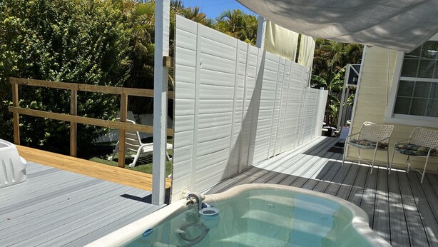 Una piscina con cubierta de madera, cerca blanca y mobiliario exterior.