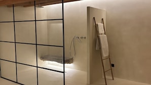Ein modernes Badezimmer mit Glastrennwand, einer Holzleiter und einem Duschbereich.