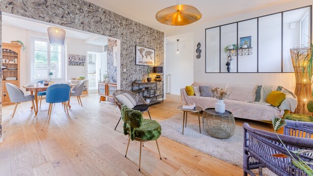 Un salon spacieux avec un mur en marbre, un grand canapé et un coin repas agrémenté de meubles en bois.