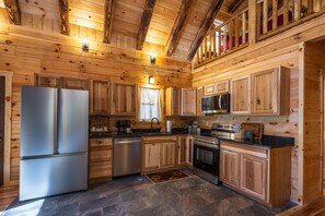 A wooden cabin-style kitchen with a refrigerator, stove, microwave, and wooden cabinets.
