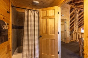 A wooden cabin interior with a shower area, a door leading to another room, and a staircase.
