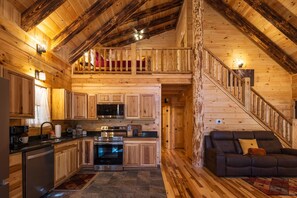 Interior de una cabaña de madera con cocina, comedor y un dormitorio en la buhardilla.