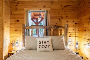 Une pièce de cabane en bois comprenant un lit, une fenêtre et une table de chevet avec une lampe.