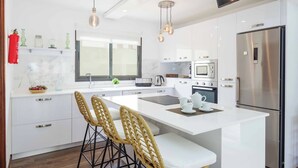 A modern kitchen with white cabinets, stainless steel appliances, and a central island with bar stools. - Villa Lanzabur - Three Bedroom Villa, Sleeps 6 (Teguise)