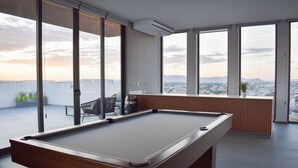 Ein Billardtisch in einem Raum mit großen Fenstern und Blick auf eine Stadtlandschaft.