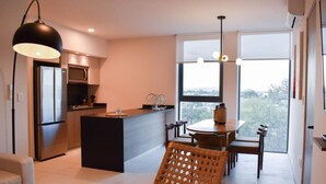 Eine moderne Küche mit einer zentralen Kochinsel, einem Essbereich mit rundem Tisch und Stühlen sowie einem großen Fenster mit Aussicht.