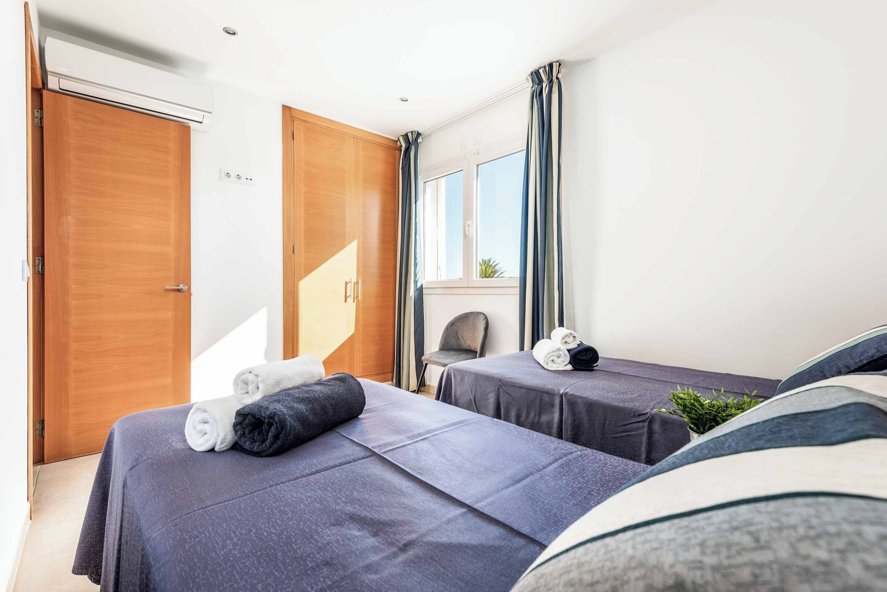 Habitación de hotel con dos camas, un armario de madera, una ventana con cortinas y una planta pequeña sobre la mesita de noche.