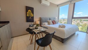 Un dormitorio moderno con una cama grande, una mesa de comedor con sillas y vistas a la ciudad.