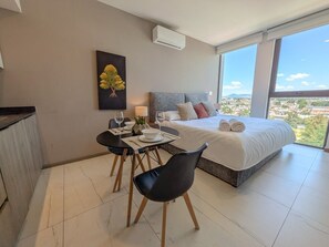 Une chambre moderne avec un grand lit, une table à manger avec des chaises et une vue sur la ville.