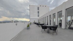 Una terraza en la azotea con mobiliario exterior y un edificio moderno al fondo.