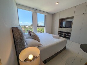 A modern bedroom with a large bed, a television, and a view through the window. - Great New Apartment close to Andares A (Zapopan)