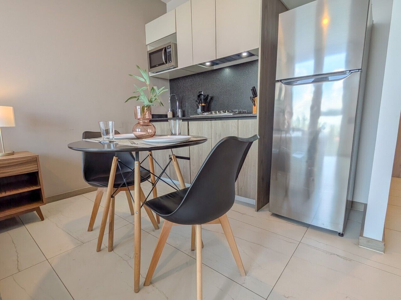 A modern kitchen with a dining table, chairs, a refrigerator, and a microwave.