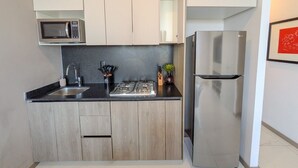 Cozinha compacta com micro-ondas, fogão, pia e geladeira de aço inoxidável.