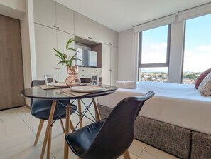 Moderni hotellihuone, jossa on ruokailutila, näköalalla varustettu sänky ja pieni keittiö.