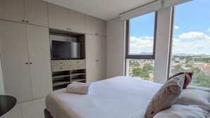 Quarto de hotel com uma cama grande, televisão e vista para a cidade.