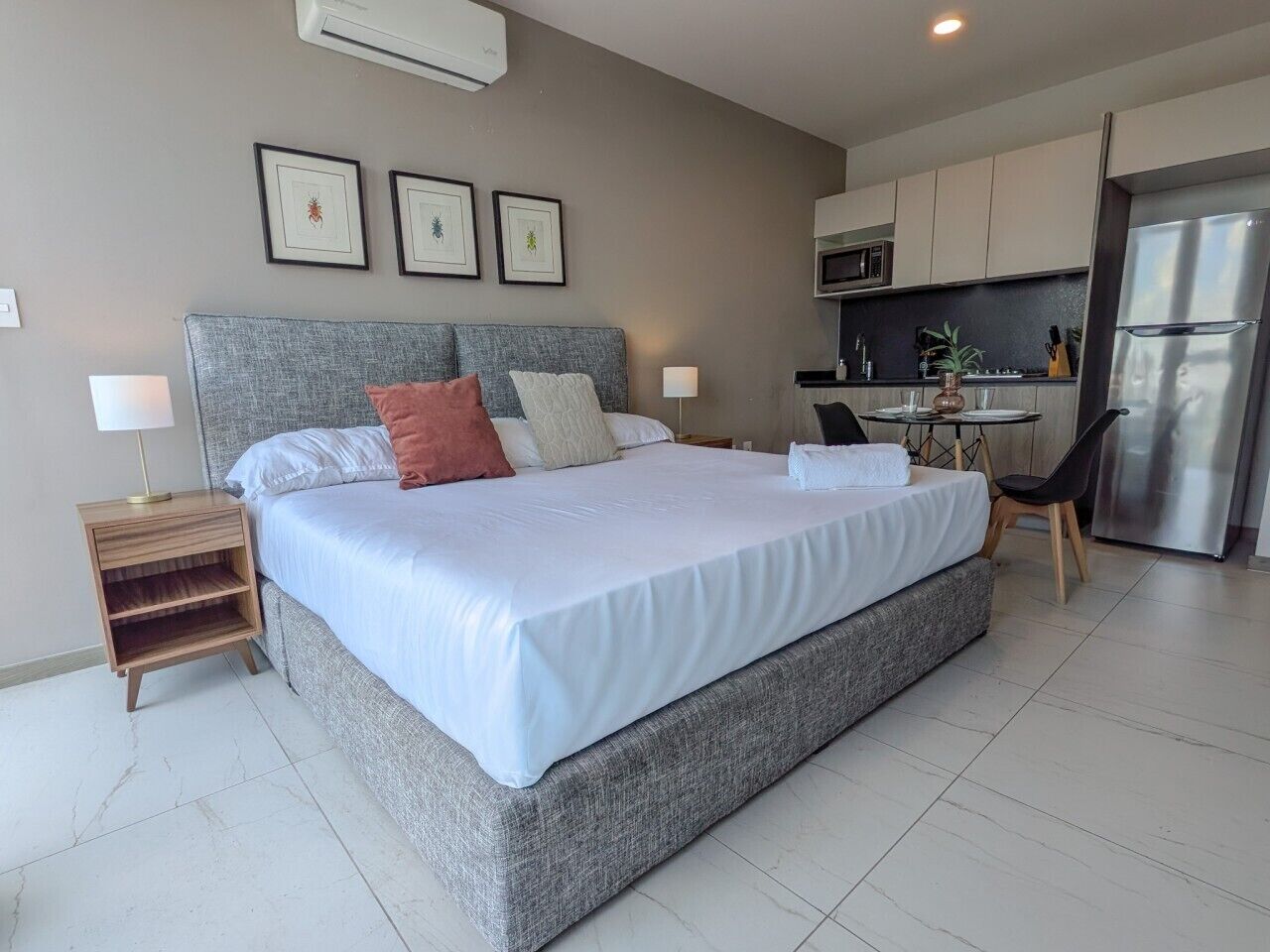 Un dormitorio moderno con una cama grande, mesitas de noche, un escritorio pequeño y una zona de kitchenette.