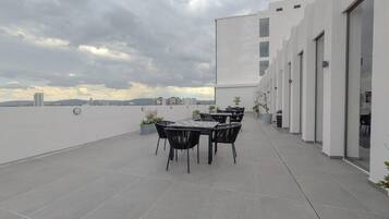 Eine Dachterrasse mit Tisch und Stühlen, Blick auf die Skyline der Stadt, und ein modernes Gebäude mit großen Fenstern.