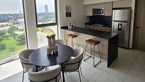 Une cuisine moderne dotée d’un grand îlot central, d’appareils électroménagers en acier inoxydable et offrant une vue sur le paysage urbain grâce à de grandes fenêtres.