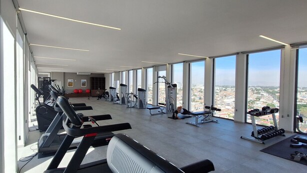 Une salle de sport équipée de divers appareils d’exercice, dotée de grandes fenêtres et offrant une vue sur la ville.