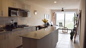 Eine moderne Küche mit Granit Arbeitsplatten, Edelstahlgeräten und einer großen Kochinsel. Es gibt einen Essbereich mit Tisch und Stühlen sowie einen Balkon mit Aussicht.
