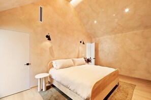 Un dormitorio moderno con una cama grande, una mesita de noche pequeña y una puerta blanca.