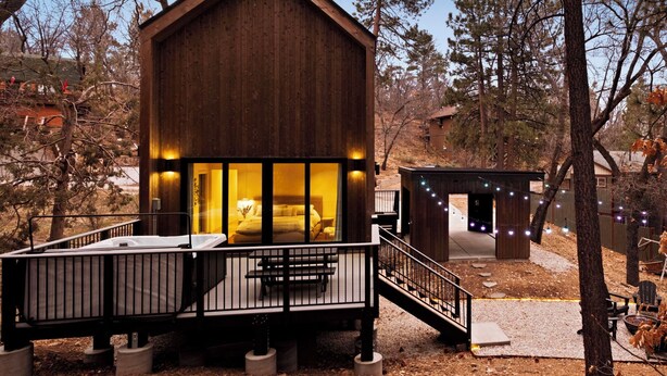 A wooden cabin with a balcony and a small deck area, surrounded by trees.