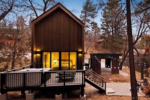 Una cabaña de madera con balcón y una pequeña terraza, rodeada de árboles.