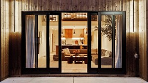 A wooden exterior with a sliding glass door leading to a living area with a sofa, coffee table, and a dining table.