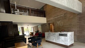A spacious lobby with a high ceiling, a reception desk, a seating area with a sofa and chairs, and a patterned rug.