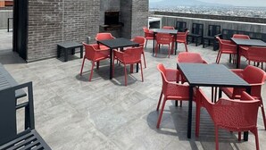 An outdoor patio with red chairs and tables, a brick wall, and a view of the cityscape.