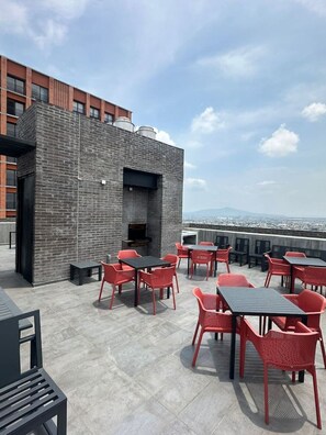 An outdoor patio with red chairs and tables, a brick wall, and a view of the cityscape. - New Loft with incredible view in YU Country 1507B (Guadalajara)