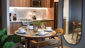 A modern kitchen with wooden cabinets, a microwave, and a refrigerator. There is a dining table set with plates, glasses, and a vase with flowers. - 24th floor with the best view of Guadalajara (Guadalajara)