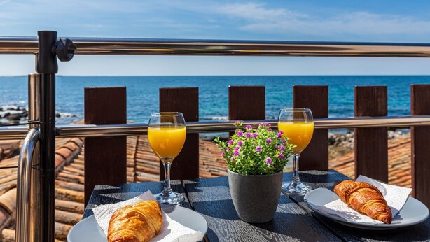 A table with croissants, orange juice, and a flower arrangement by the sea. - Beachfront Escape in Rovinj - Sea Studio (Rovinj)