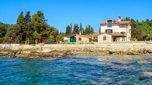 A coastal property with a stone wall, clear blue waters, and a two-story building with a tiled roof. - Beachfront Escape in Rovinj - Sea Studio (Rovinj)