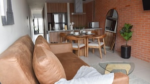 Un salon moderne avec un canapé marron, une table basse en verre et un coin repas comprenant des chaises en bois et une table blanche.