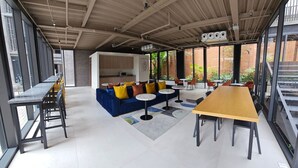 Un espace intérieur spacieux avec une longue table, un canapé bleu agrémenté de coussins colorés et plusieurs petites tables rondes.