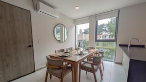 Een moderne eetruimte met een houten tafel voor vier personen, omringd door stoelen, een grote spiegel en uitzicht op het buitenlandschap via een schuifdeur.