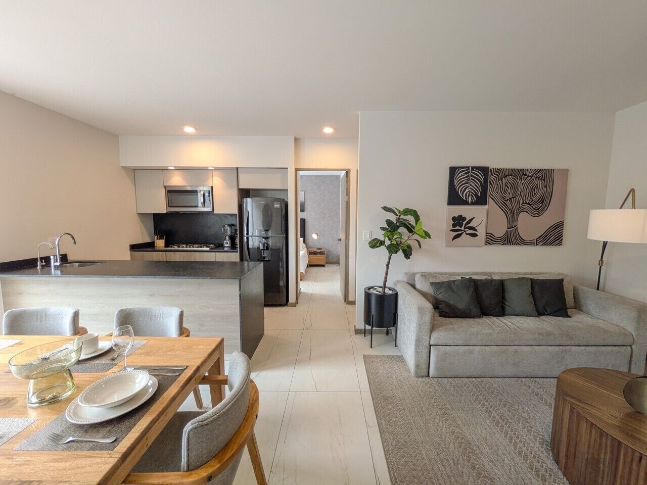 Un salon moderne avec un canapé, une table à manger dressée pour deux personnes et une cuisine en arrière-plan.