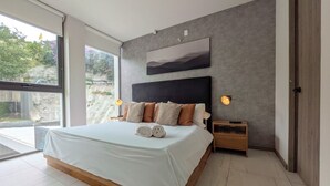 Un dormitorio moderno con una cama grande, cabecera, lámparas de noche y vistas a través de un ventanal.