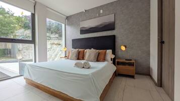 Une chambre moderne avec un grand lit, une tête de lit, des lampes de chevet et une vue dégagée sur l’extérieur grâce à une grande fenêtre.