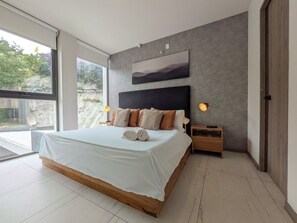 A modern bedroom with a large bed, a headboard, bedside lamps, and a view through a large window. - Amazing new apartment near Andares 310A (Zapopan)