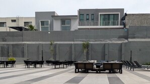 An outdoor seating area with tables and chairs, a wooden bench, and a building in the background.
