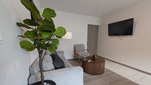 A modern living room with a grey sofa, a round coffee table, a potted plant, and a flat-screen TV mounted on the wall.