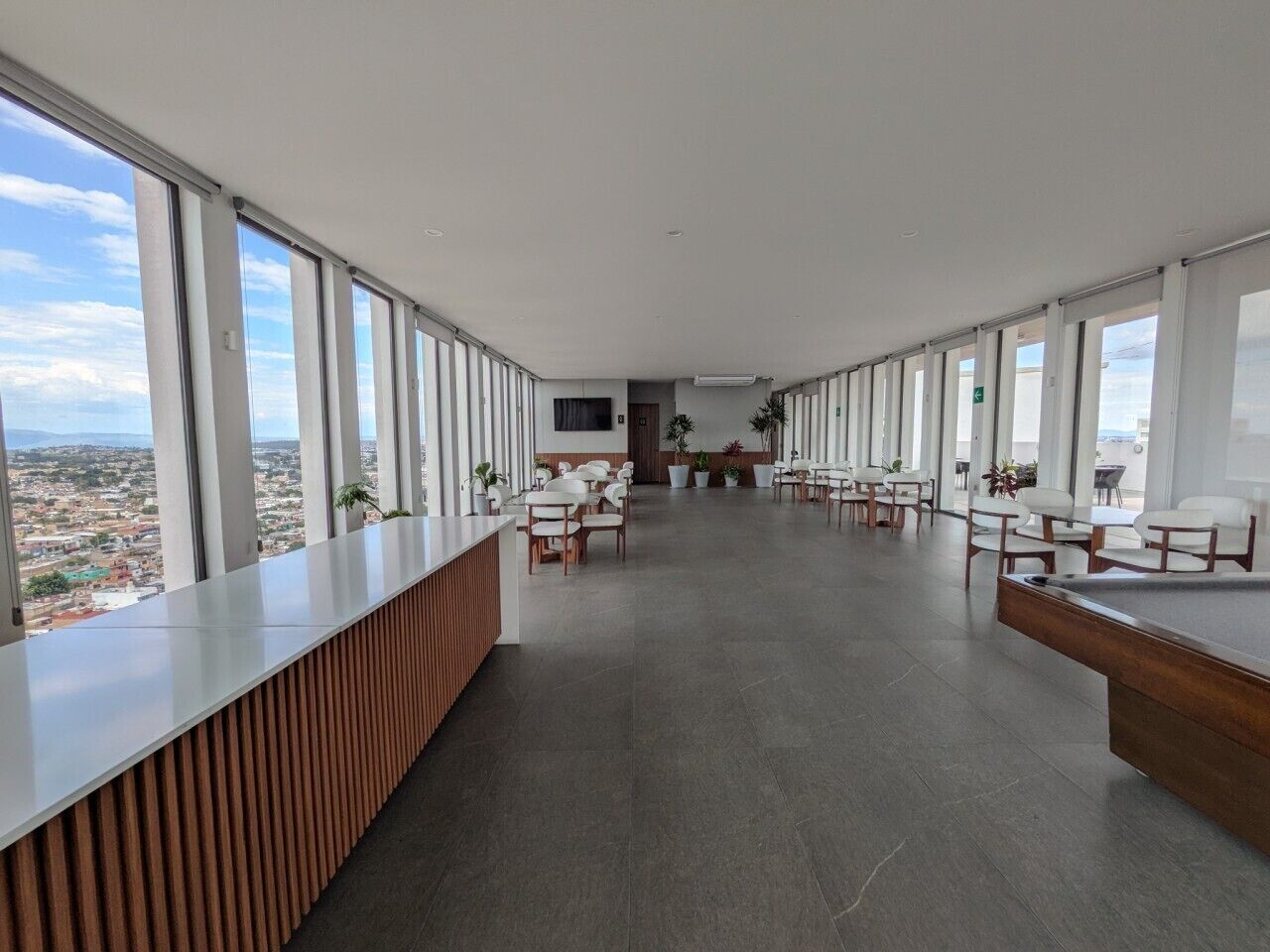 A spacious, modern hotel lobby with a long reception desk, multiple seating areas, and large windows offering a city view.
